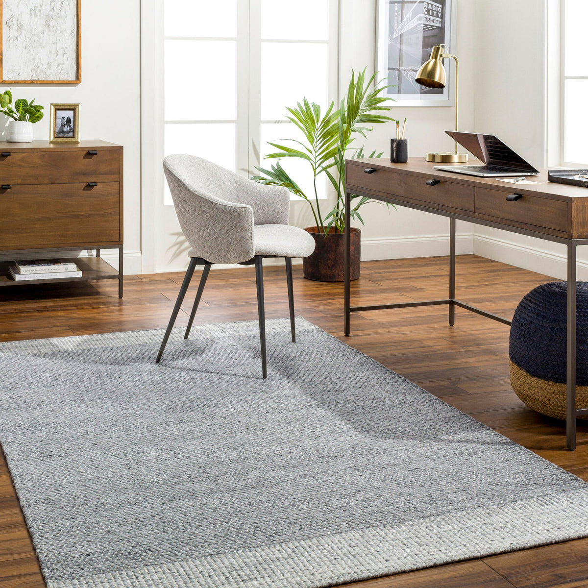 Home office with a grey and ivory bordered rug, desk and upholstered chair