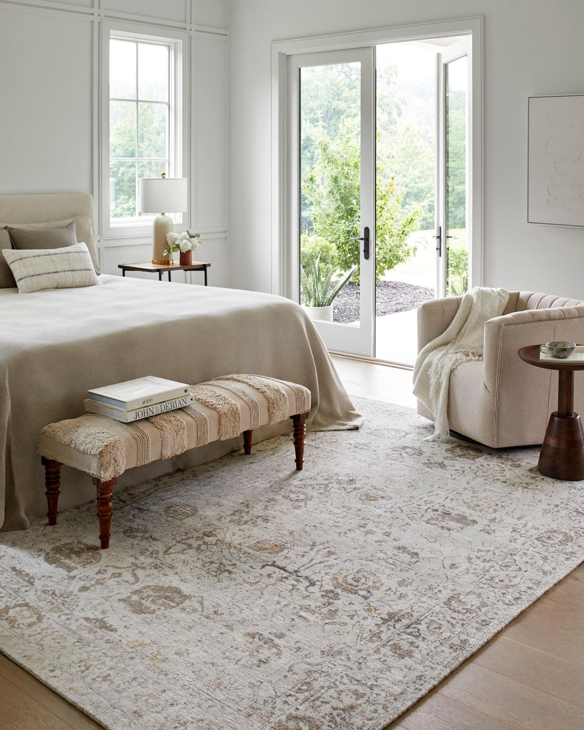 Bedroom with a pale distressed rug, upholstered bench and armchair