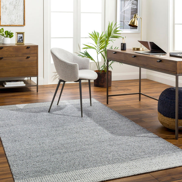 Home office with a grey and ivory bordered rug, desk and upholstered chair