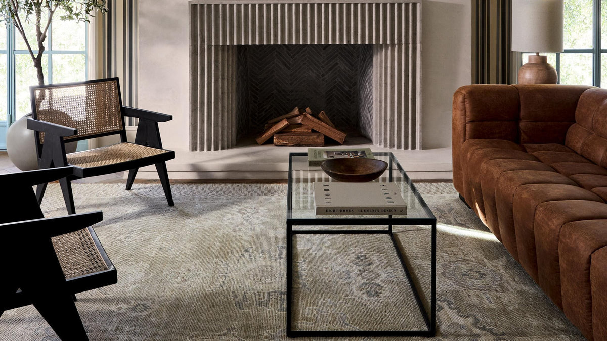 Living room with a stone fireplace, round mirror, cognac leather sofa and a soft green-grey wool rug