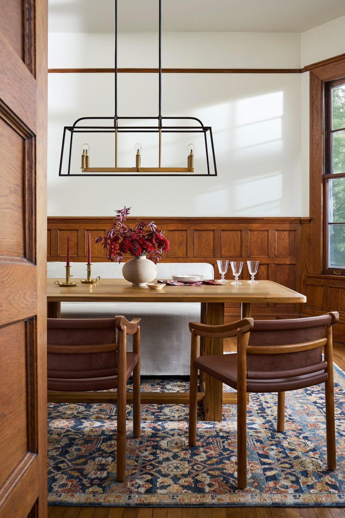 Dining room with a linear black chandelier, wood table and a traditional rug